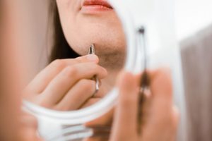 Woman plucking chin hairs caused by PCOS 